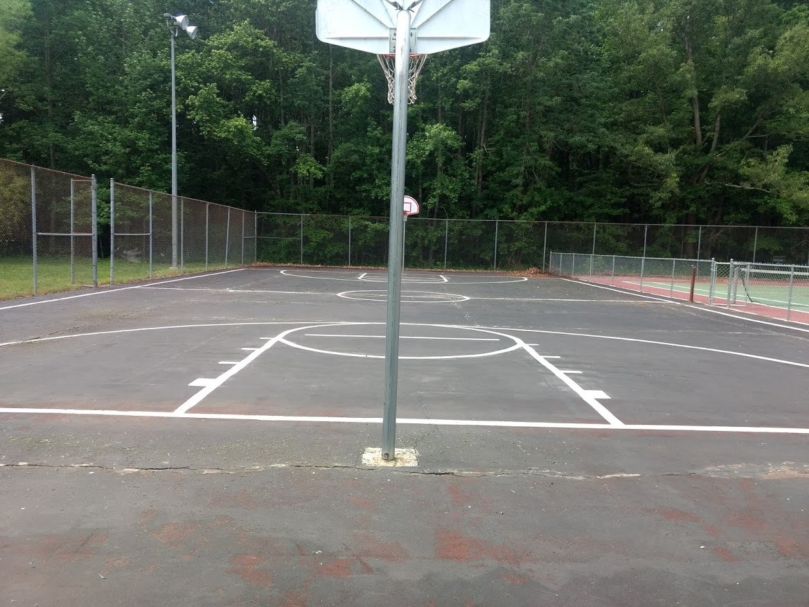 Worn basketball court with faded, patchy asphalt before resurfacing